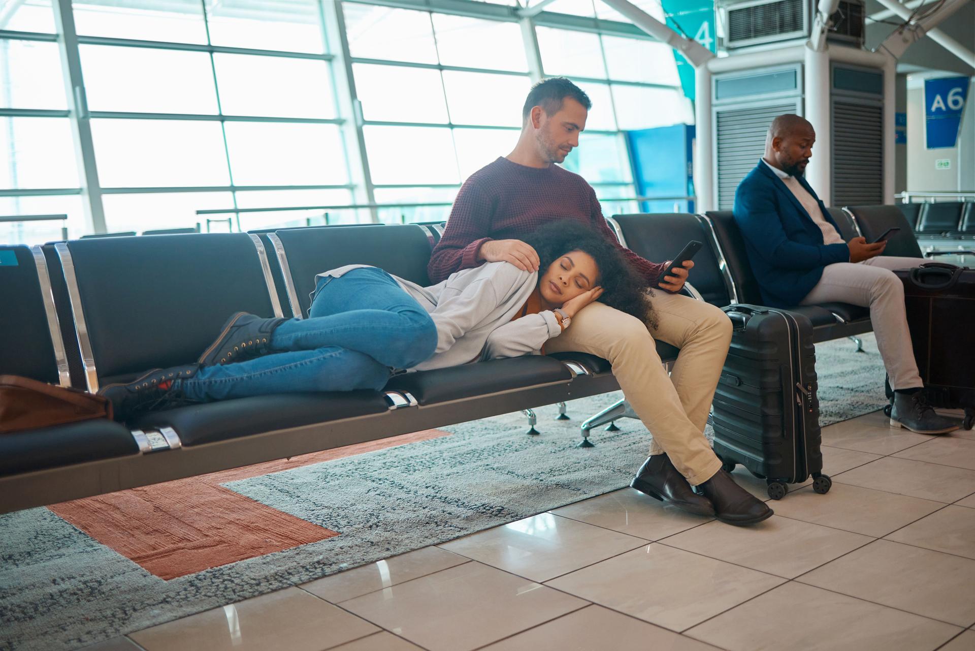 Fatigué, retard et couple à l’aéroport pour un vol, attendant et assis dans le salon sur un téléphone. Immigration, détente et femme dormant avec un homme lisant sur un mobile tout en voyageant pour les vacances
