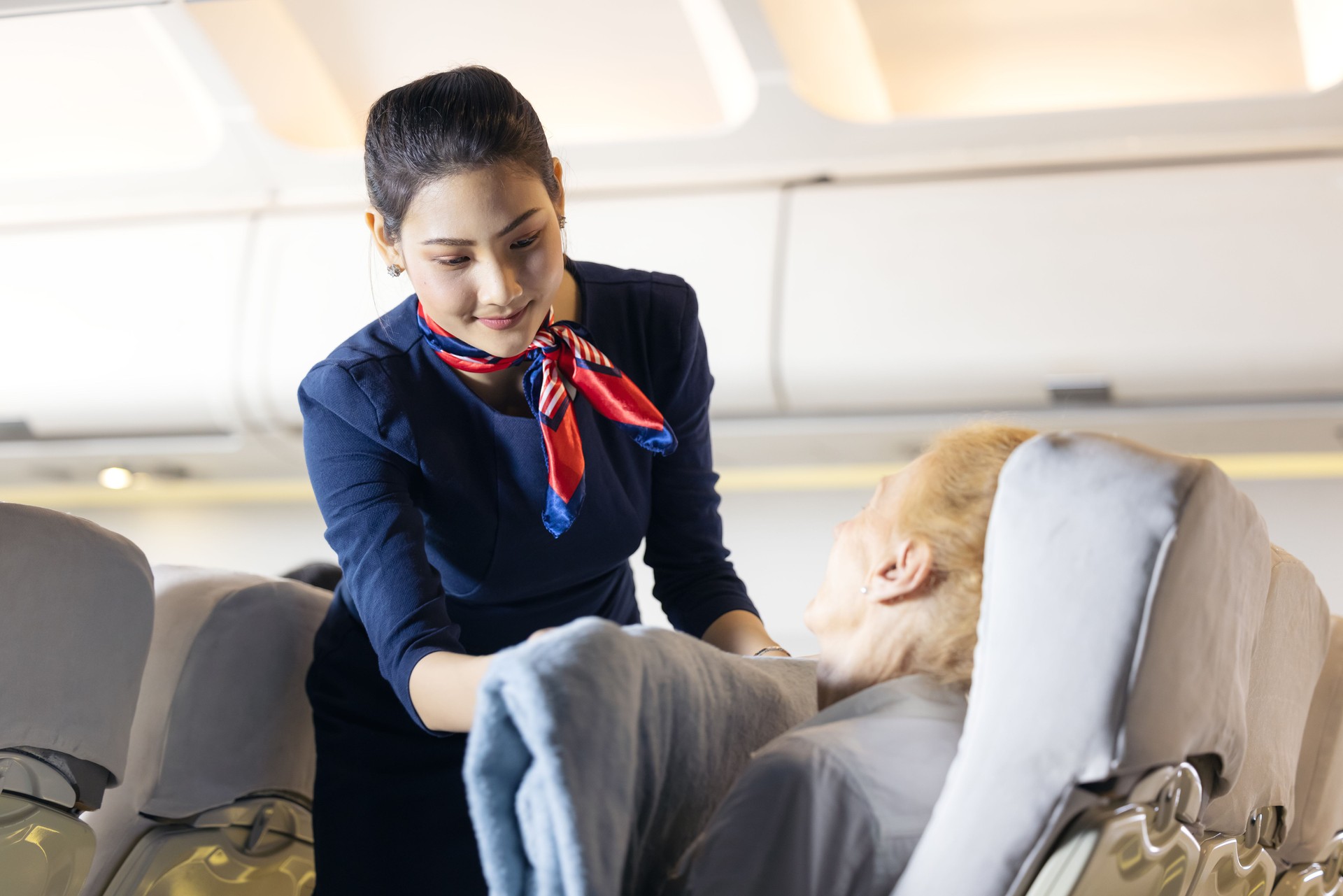 Une hôtesse de l’air a habillé une passagère âgée dormant sur le siège passager. Hôtesse de l’air s’occuper du passager. Le personnel de cabine donne le service à un passager dans un avion.
